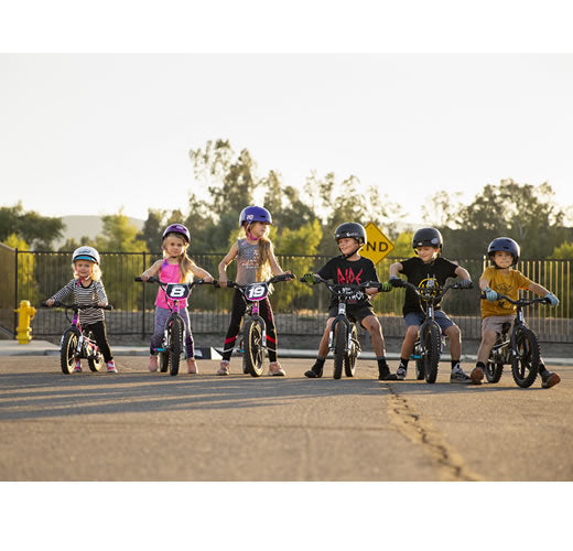 Six children in helmets ride colorful stacyc balance bikes on a paved road comparing 16edrive models